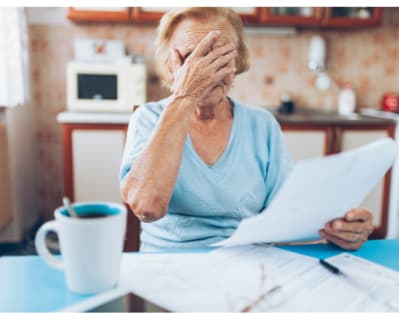 Lady sitting in kitchen looking at bills and looking worried